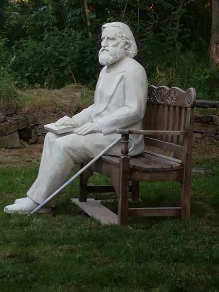 Скулптура на Учителя Петър Дънов, седнал на пейка, изглед от дясно