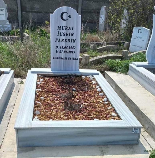 Muslim monument with a crescent moon and star, inscription in carved black letters, pedestal, tiled curb, cement path, concrete base