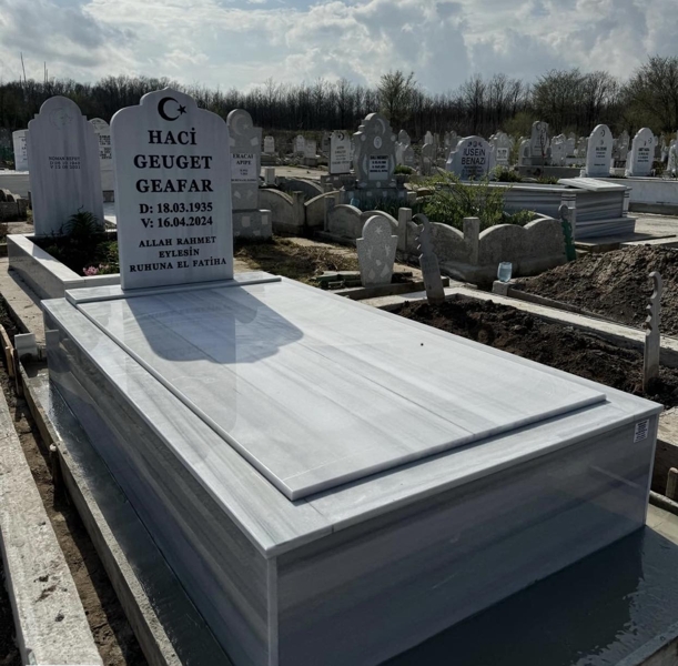 Muslim monument in the shape of a mosque with a crescent moon and a star, inscription in carved black letters, pedestal, roof slab, high tiled curb, concrete base