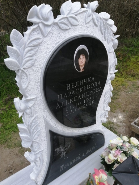 Паметник от светлосив мрамор с клонки и цветове рози, залепени черни плочи със снимка, надписи и гравирано ангелче, изглед отляво